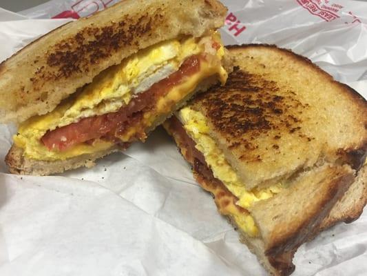 Sourdough breakfast sandwich with bacon, cheese, egg and tomato.