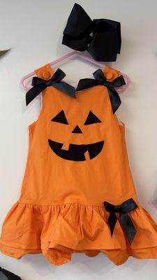 Romper dress all ready for Halloween. A happy pumpkin with bows and buttons on each shoulder and a bow on the bottom left side.