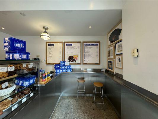 Levain Bakery Harlem counter with fresh-baked cookies, breads, and menu boards, featuring stainless steel finishes and cozy seating.