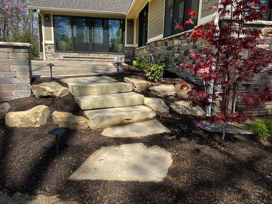 Natural stone steps leading to a paver patio with columns