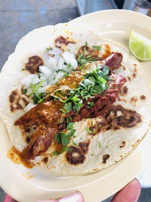 Taco- birria meat on a hand made tortilla topped with cilantro, onion and red salsa.