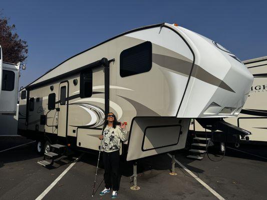 A Cougar 5th wheel with a person standing in front smiling.