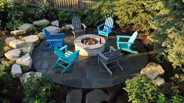 Gabouri limestone-clad gas fire pit in an Ashlar pattern bluestone patio, with outcropping boulders that retain soil and offer more seating.