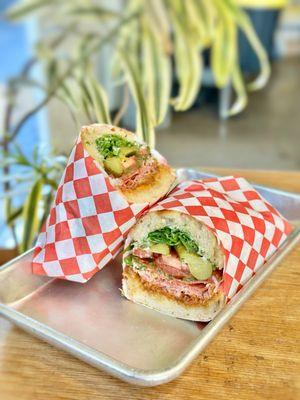 SPICY SANDO Spicy salami, romesco, pickled jalapeños, cornichons, tomatoes, chimichurri, arugula, Beemster cheese, herbed aioli