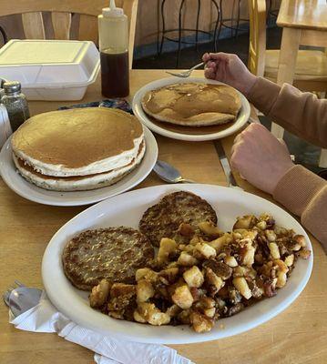 Full stack of pancakes with side of sausage and home fries