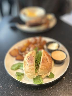 Alma Breakfast Sandwich: farm egg, bacon, white cheddar, baby arugula, spicy mayo, everything spice brioche bun, breakfast potatoes | $24