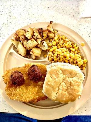 Catfish half hidden by biscuit, German fries, hush puppies and corn.