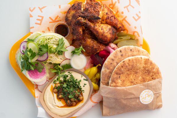 Our most popular menu item: the quarter plate with rotisserie chicken, wedge salad, hummus, pickles, pita, chili oil, and garlic sauce.