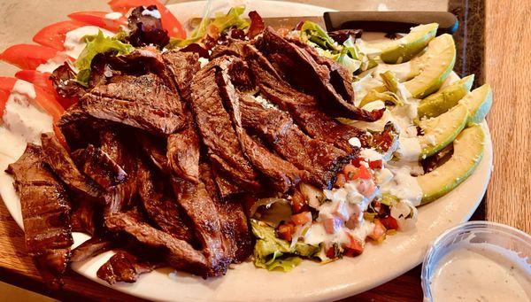 Carne Asada Salad with slices tomatoes and avocados on a bed of lettuce with ranch dressing.