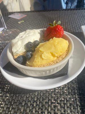 Lemon dessert with Graham cracker garnish, fresh berry compote surrounded by blueberries and a strawberry garnish