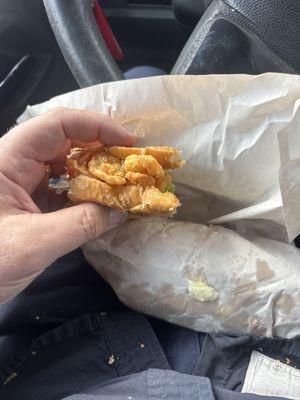 A fried shrimp poboy with shrimp over flowing the bun .