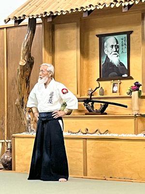 Saotome Sensei, founder of Aikido Schools of Ueshiba, pictures of O'Sensei and Shindai founder Dennis Hooker in background, June 2023