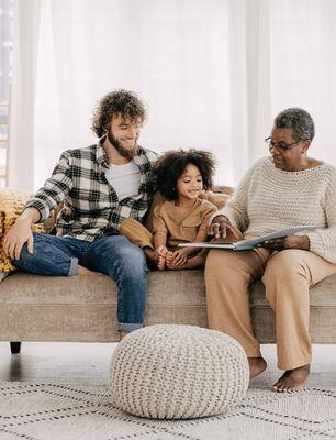 A warm, inviting scene of a multigenerational family sitting together on a couch, sharing a book and smiling. The image conveys connection,