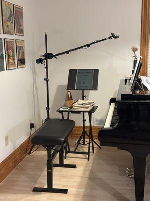 The camera boom stand in the corner of my teaching studio, holding my webcam above the keyboard.