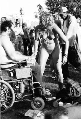 Pravda naked as usual wearing love beads. Pravda had just taken off the shirt of the man in wheelchair. This is in People's Park. Tom Brody