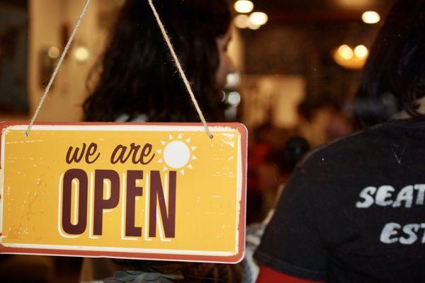 Open sign with open mic night performers in the background.