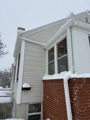 Large downspout leaning on porch bricks. Small horizontal downspout going from the large roof to the porch.