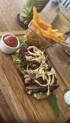 Steak sandwich with Maui onion crisps and arugula served open face on sourdough bread with fries.