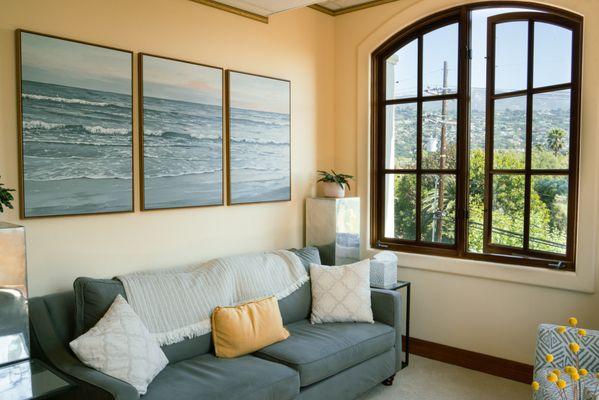 Peaceful therapy office with ocean artwork and natural light for a calming session environment.