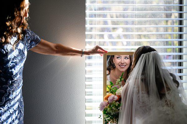 Mother holds a mirror for her daughter for a look right before walking down the aisle, we capture the whole story, not just poses.