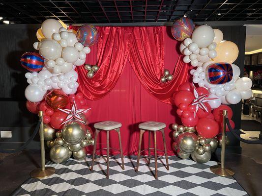 A photo op at the circus, complete with a gold, red, and white balloon garland and checkered rug.