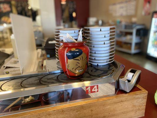 The old sushi belt is no longer in use, but it's still there. There's a stack of the old plates that were once used on the belt.