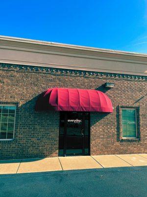 blue sky, red canopy over a glass door with everyday CFO's logo. brown brick building.