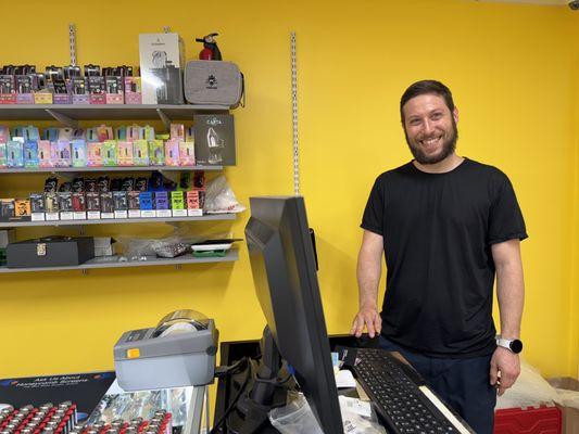The proprietor in front of the bright yellow, cheery wall and a selection of vibey stuff for chillin' ....
