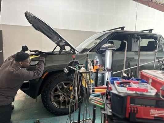 Lenny repairing a dent in the front left Rivian R1T fender.
