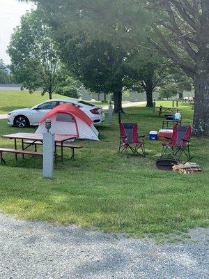 View of our campsite, with plenty of shade, a fire it, water spicket, picnic table, and electrical box with attached campsite light.