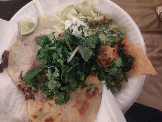 Two quesadillas. Al pastor and asada with a side of cilantro, guacamole, cabbage, sour cream and two salsas (green and red).