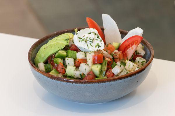 A salad sits on the table with romaine lettuce, chopped vegetables, avocado, burrata cheese, and honey-lemon dressing.