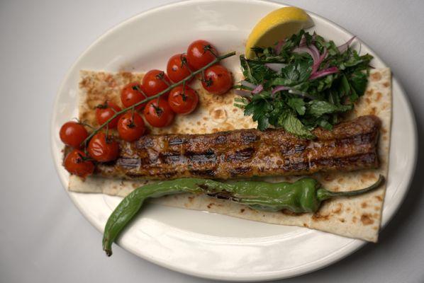 ADANA KEBAB: spicy hand chopped skewered grilled lamb, served on top of pita bread and onion salad