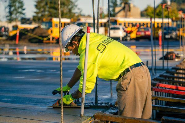A Standard Commercial Construction crew member smooths freshly poured concrete, ensuring a level, durable foundation for the project.
