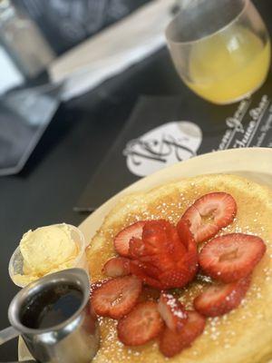 One pancake topped with strawberries and a mango mimosa
