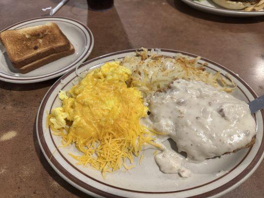 Country fried steak with gravy, eggs scrambled with cheese, hashbrowns, and white toast