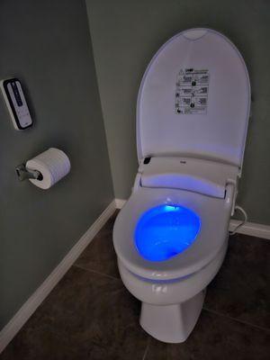The Smile Memory bidet on the toiletseat with the blue LED light and remote mounted on the wall.