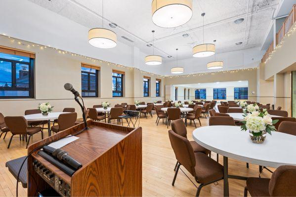 Spacious ballroom featuring a podium with mic, projector, and elegant banquet seating. Ideal for conferences, trainings, and celebrations.