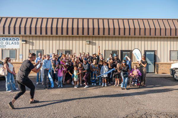 A vibrant ribbon-cutting ceremony with community members gathered around, cheering as the ribbon is cut, symbolizing unity and support.