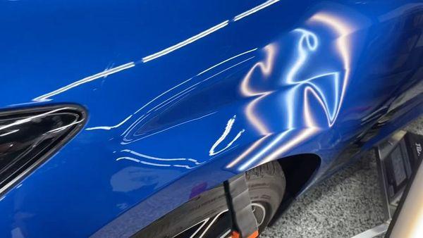 A noticeable dent is visible on the bright blue fender of a car, reflecting light and showing the distorted body line.