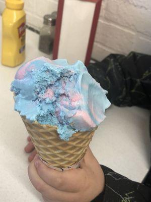 Waffle cone double dip with strawberry on bottom and cotton candy on top with 1 bite taken out