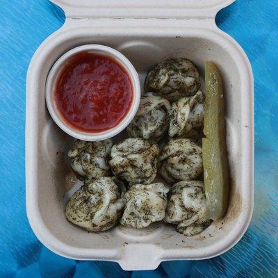Snack size pork Siberian style ("pelmeni") dumplings with Georgian chilly ("Adjika") and a pickle on the side.