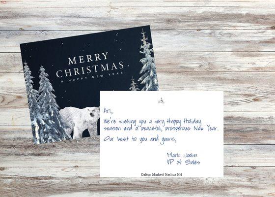 A navy blue holiday card featuring a stylized winter scene with snowy pine trees and a polar bear.