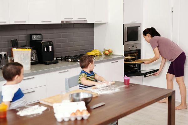 A parent bakes while kids help in a bright, modern kitchen--showing the comfort and reliability of well-working home appliances.