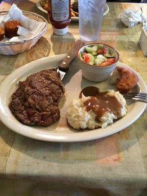 8 oz ribeye, cucumber and tomato salad, mashed potatoes and half eaten roll.