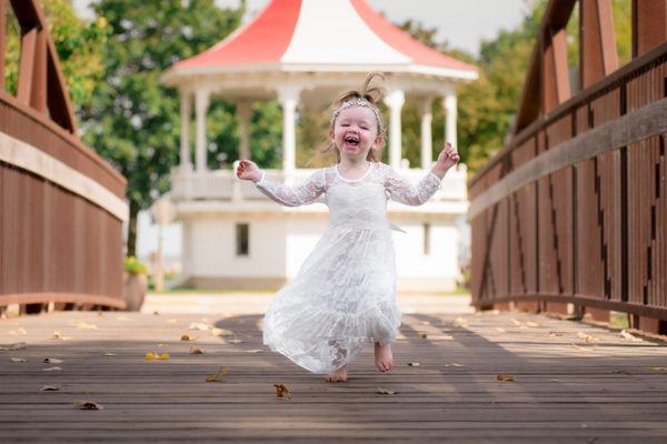 Flower girl runs down the bridge towards the camera and she's having a great time! - Oshkosh Wedding Photography