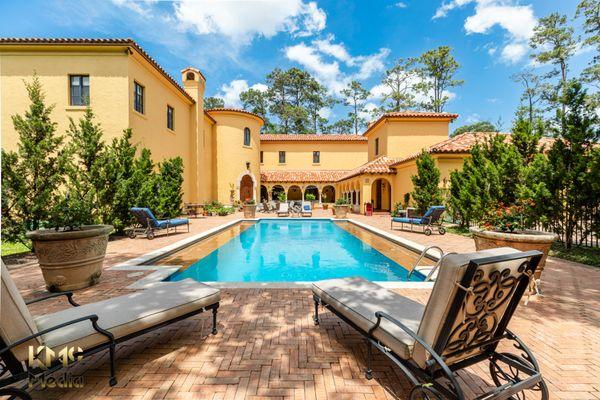 Real estate photography of residential home's exterior back landscaped with pool and sitting areas.