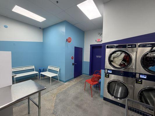 Comfortable seating throughout, including benches, café-style chairs, and a work bar with charging access