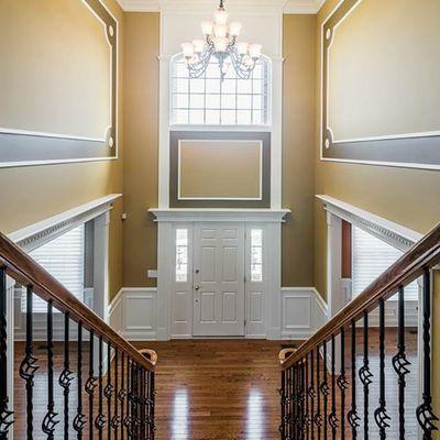 Two-story foyer woodworking enhanced with complementary painting creates a dramatic entrance way.