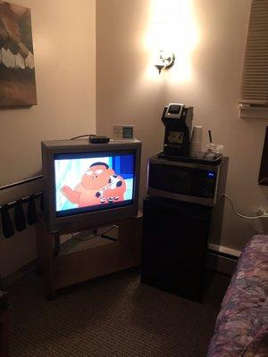 Older tv but cable box with channels, microwave, mini fridge, and coffee maker with the fixings.